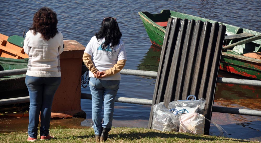 Dos mujeres esperan una embarcación que las trasladen. Ya tienen chapas de cartón y mercaderías.