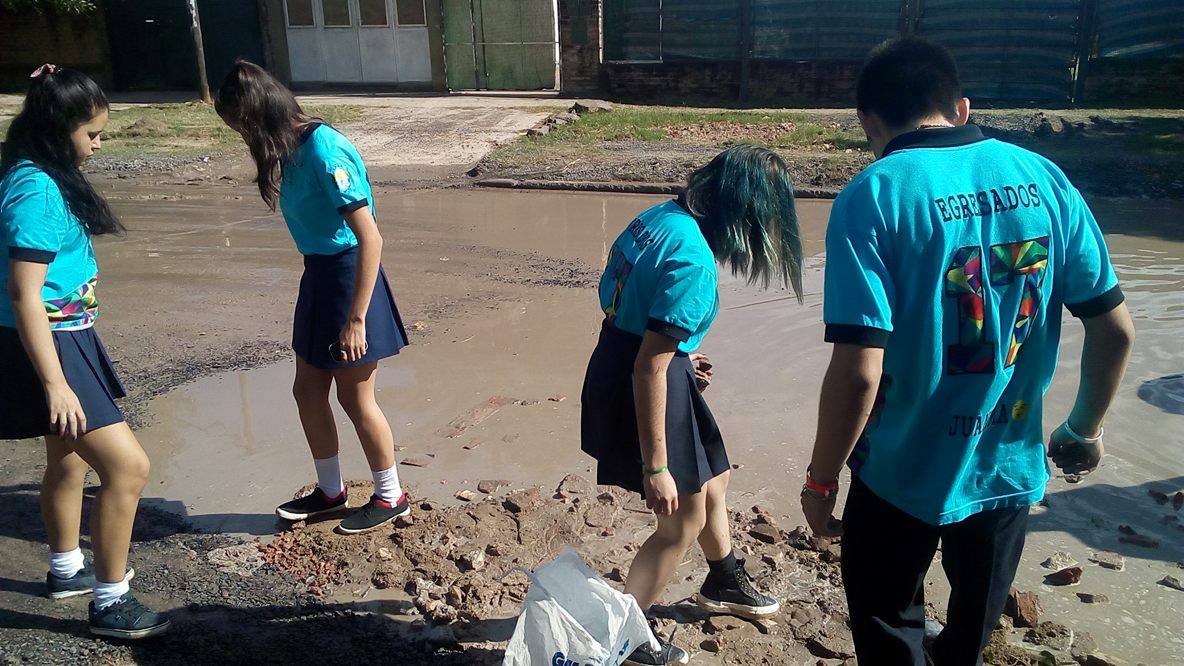 Alumnos secundarios rellenan un bache en el barrio Lote Cuatro